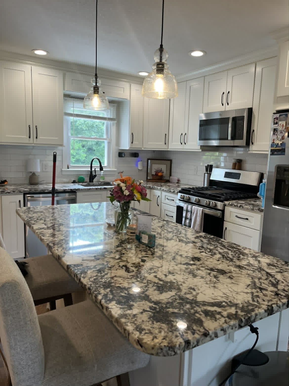 Clean white kitchen with granite island and pendant lights